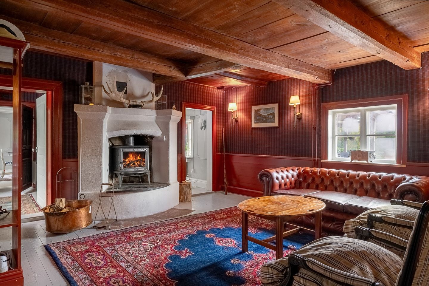 The mangårdsbyggnad lounge — wood stove, old sofas, original beamed ceiling